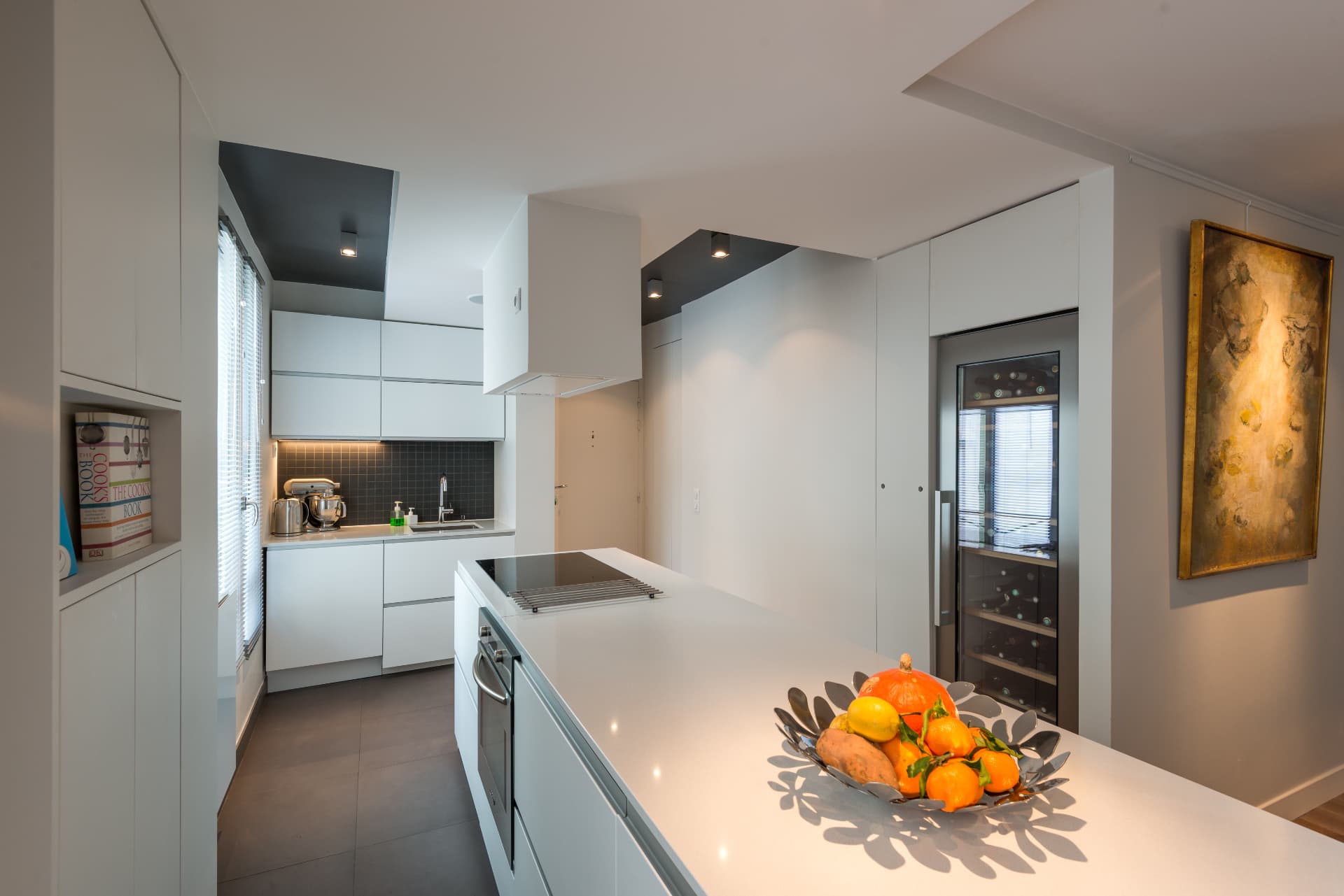 White kitchen with long island, wine fridge and dark ceiling niche