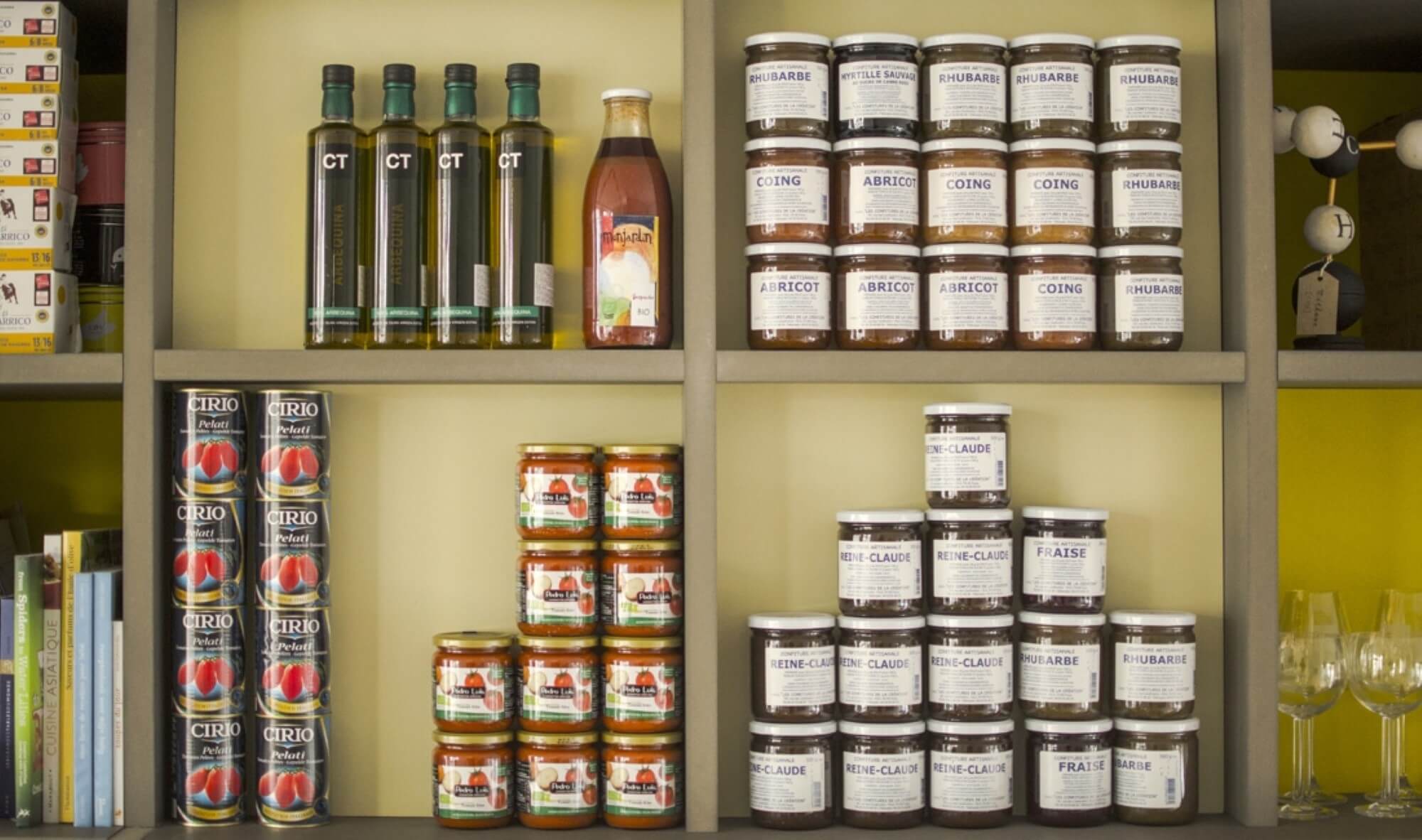 Detail of shelving compartments with olive oil bottles, artisan jams and glassware on yellow backing