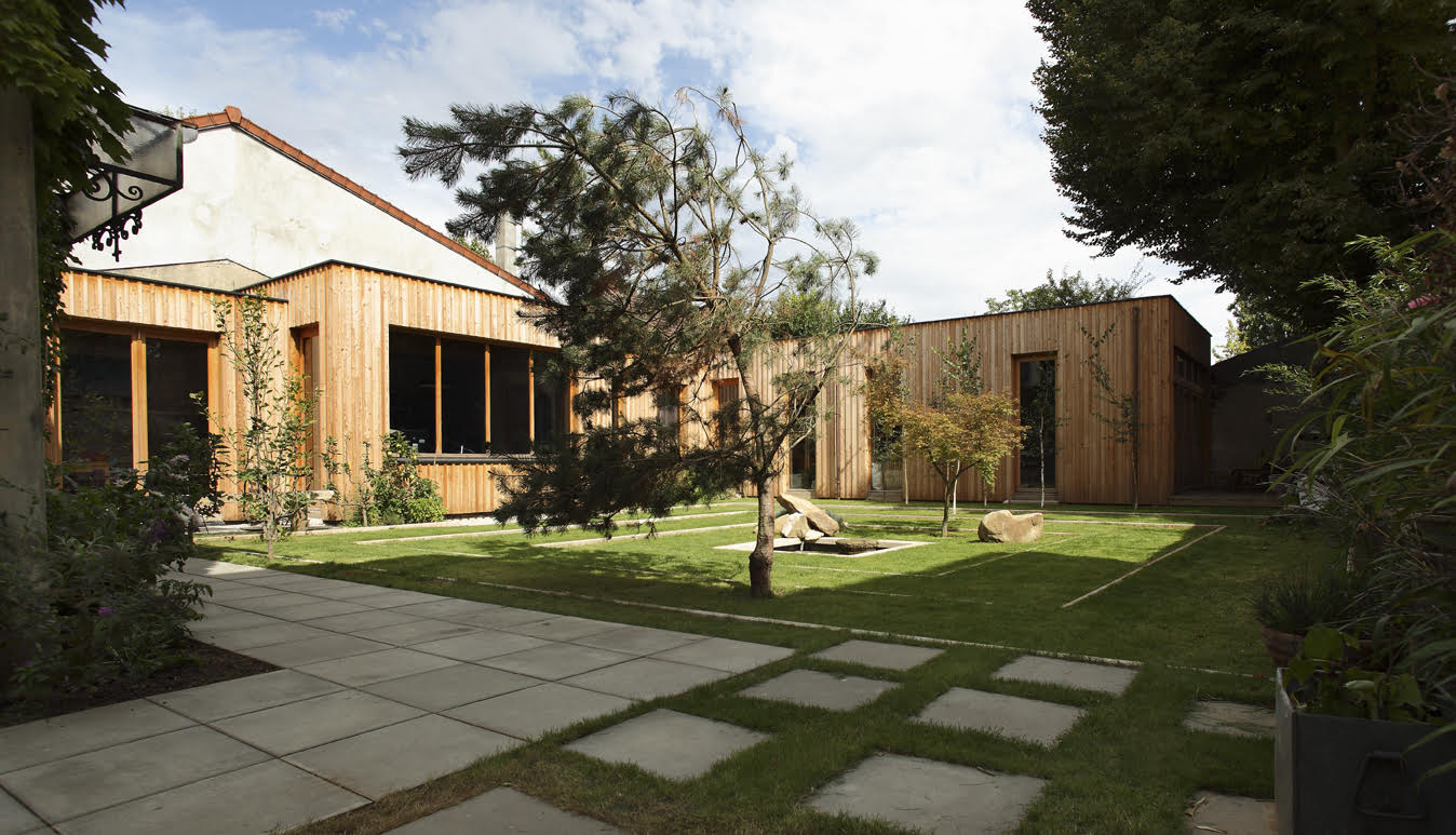 Wide garden view of the larch-clad studio with stepping-stone path, pines and stone basin