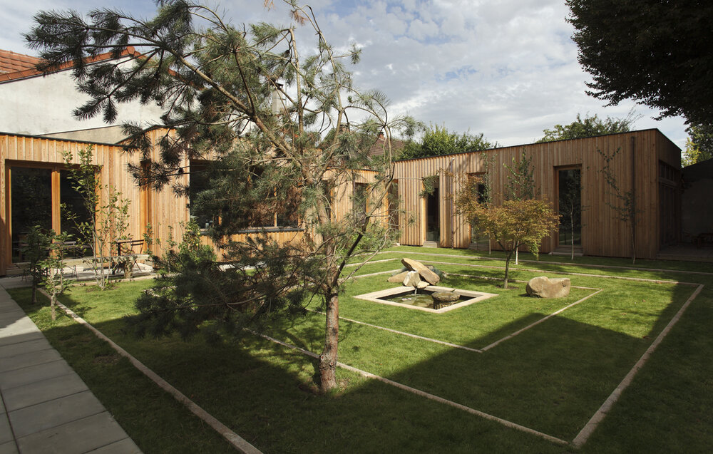 Larch-clad artist studio wrapping a garden courtyard with pine tree and stone water basin