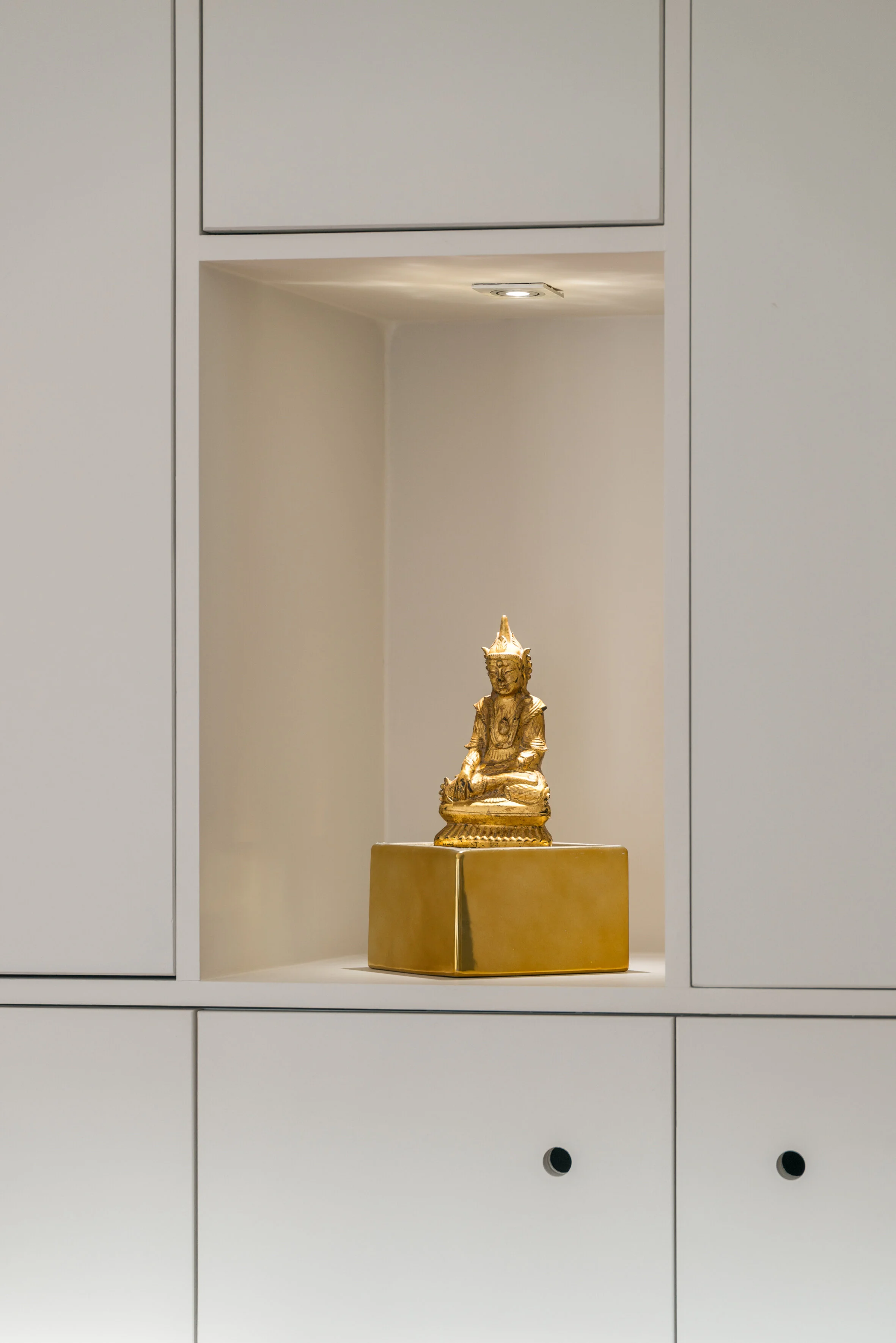 Full-height white joinery with a lit niche holding a gilded Buddha