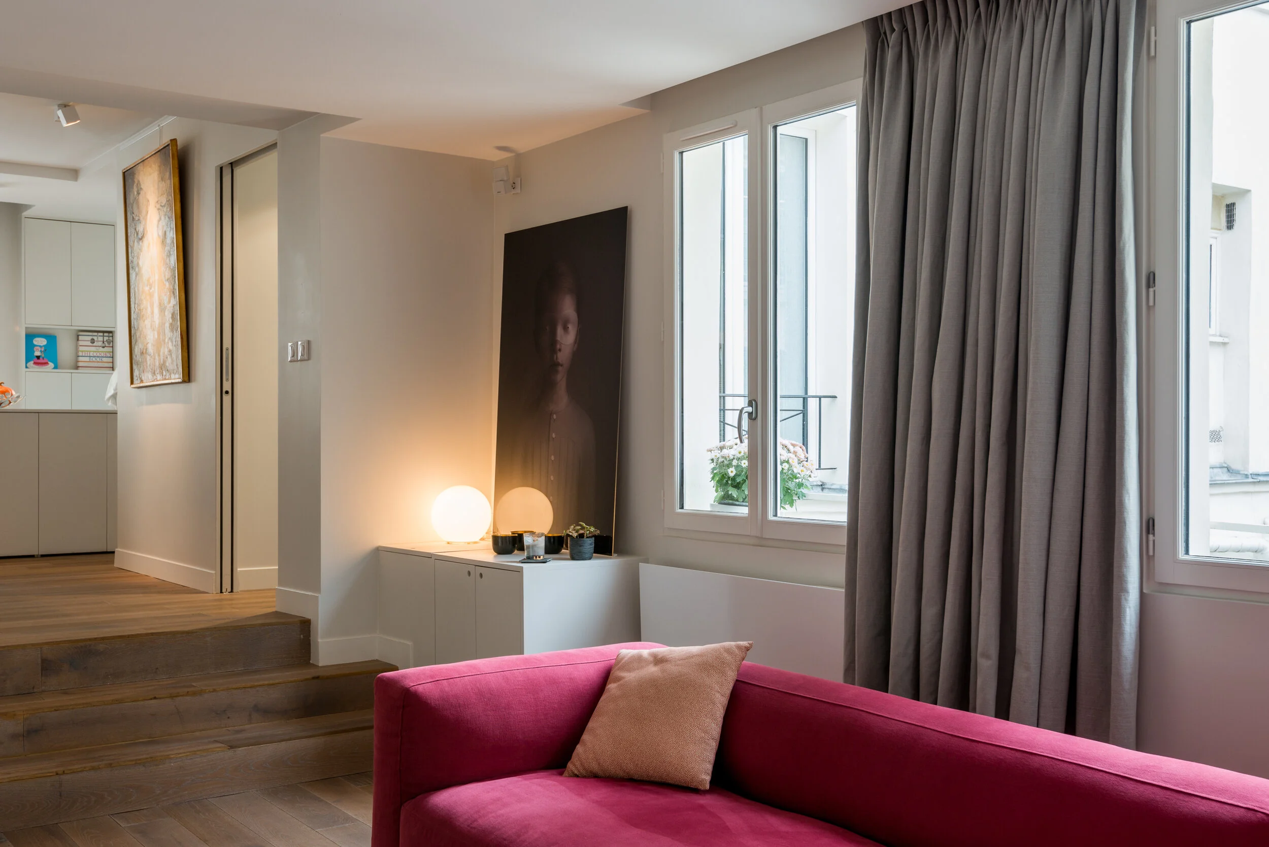 Living room with a raspberry sofa and a large portrait canvas leaning by the window, Rue de Turin