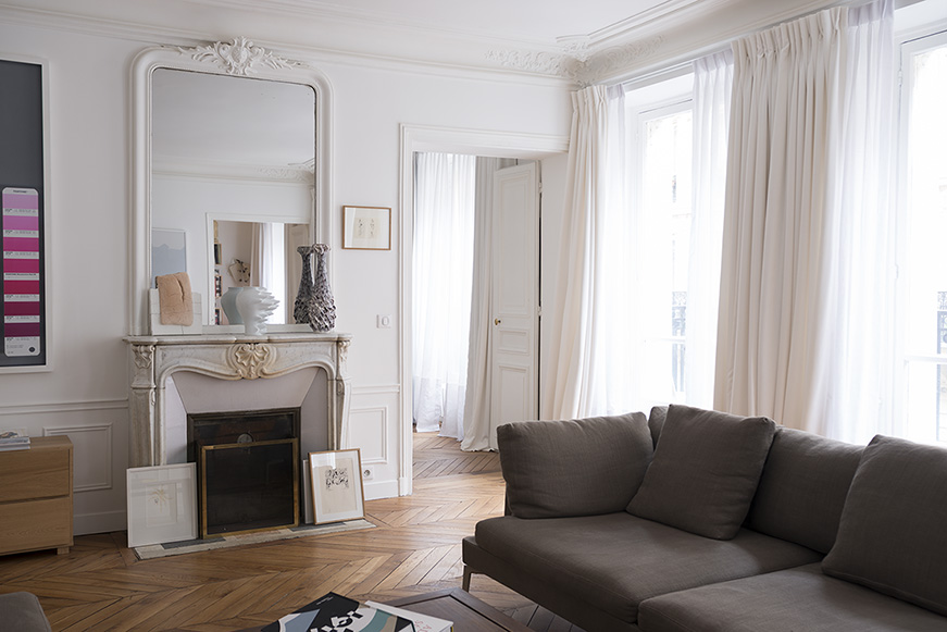 Haussmannian living room with restored marble fireplace, tall mirror and chevron parquet, Paris