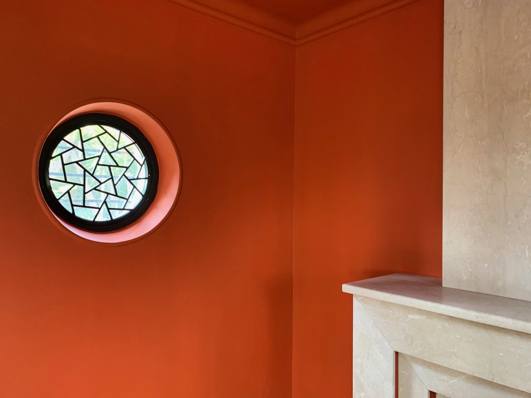 Stained-glass oculus set into a terracotta wall above the stone chimney breast