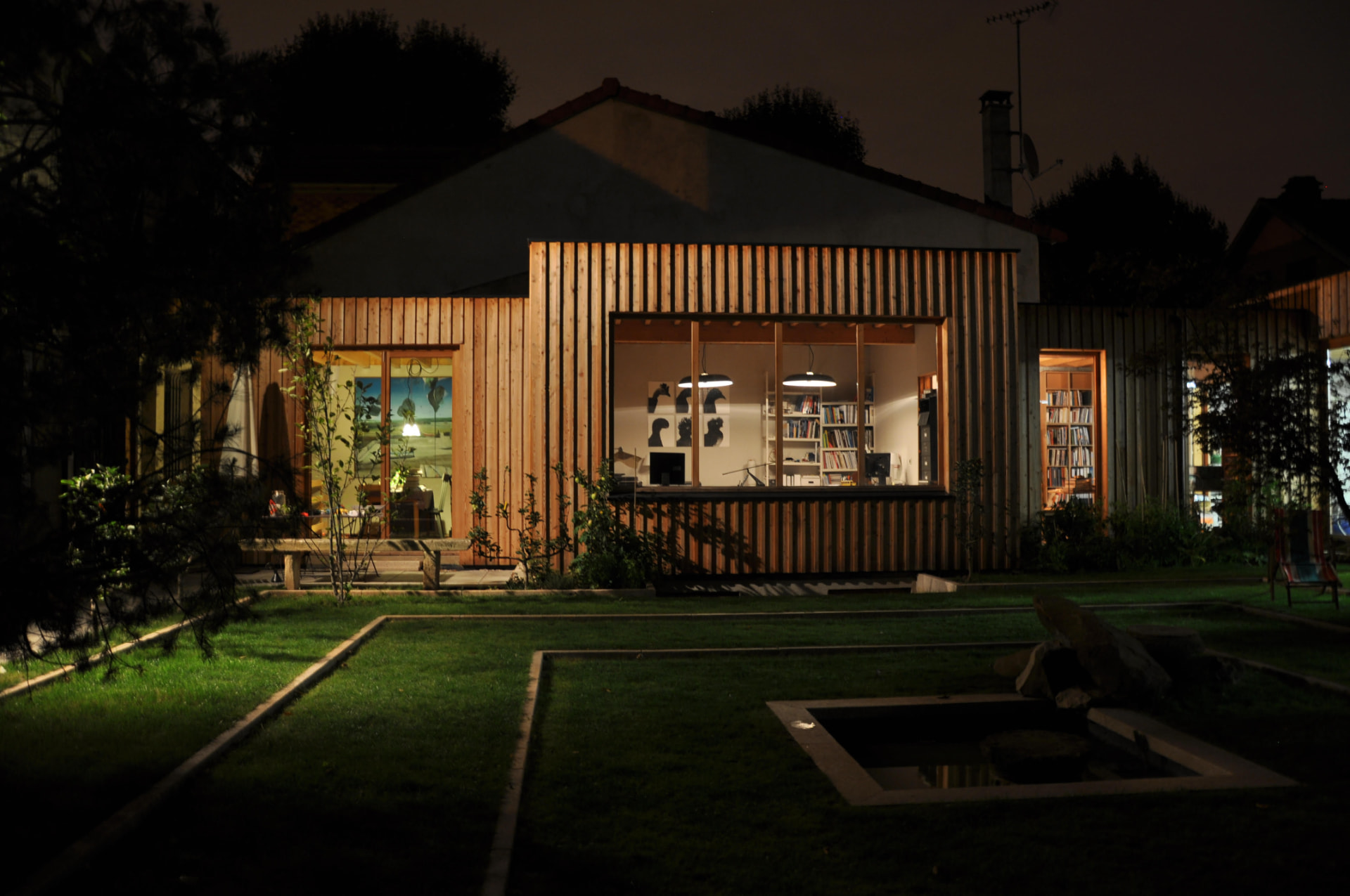 The timber studio at night, glowing from within across the dark garden