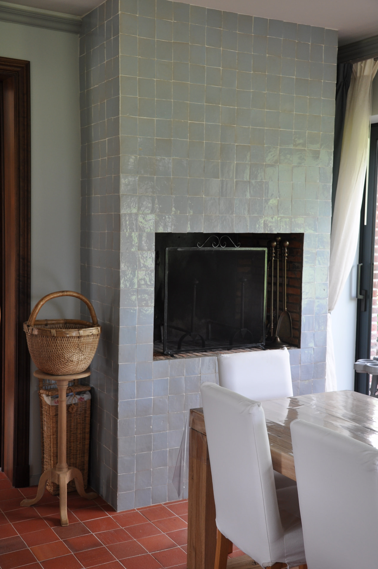Chimney breast clad in pale blue-green zellige tiles above a terracotta tiled floor