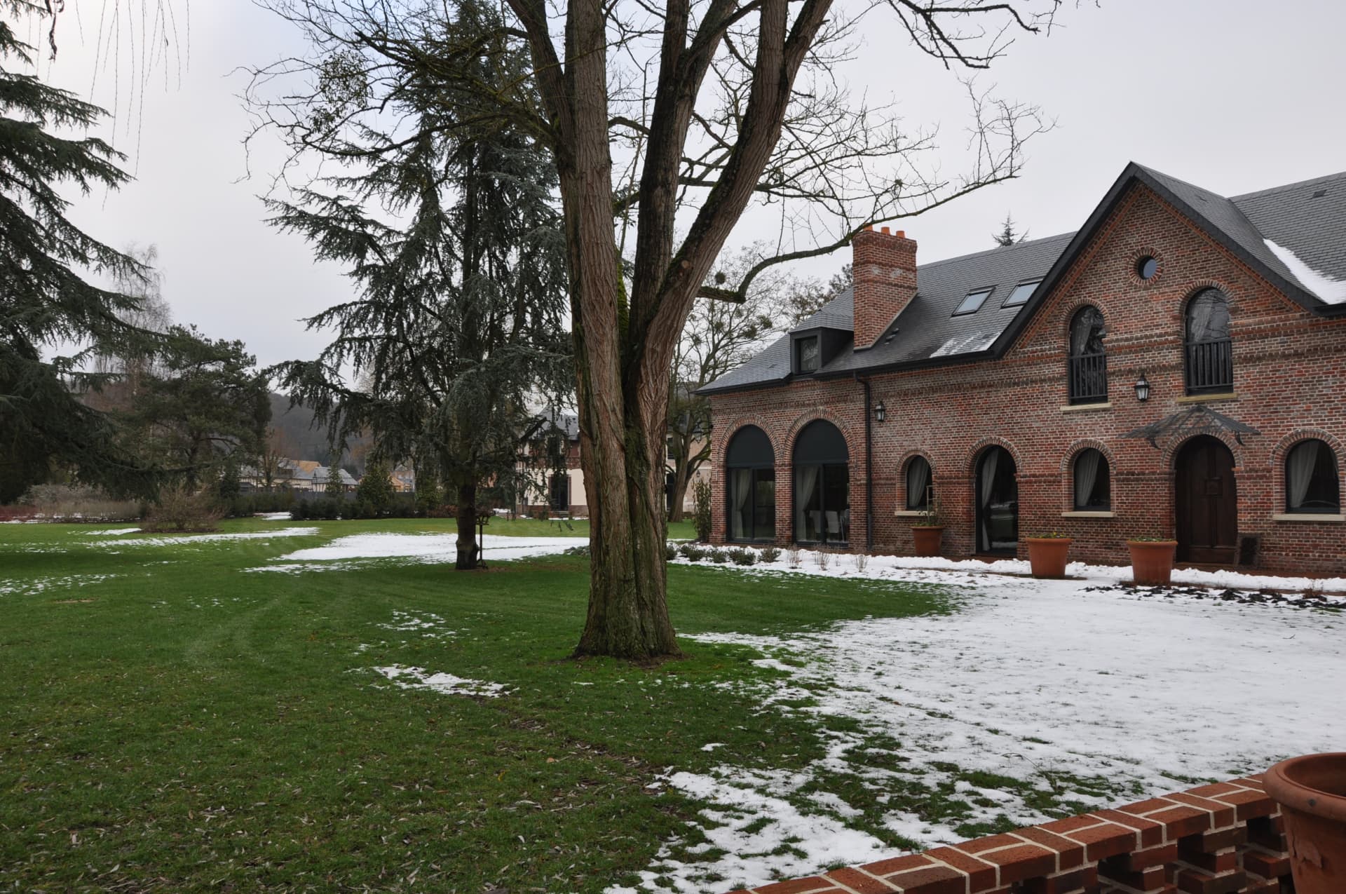 Brick manor house with slate roof seen across a snow-dusted park in winter