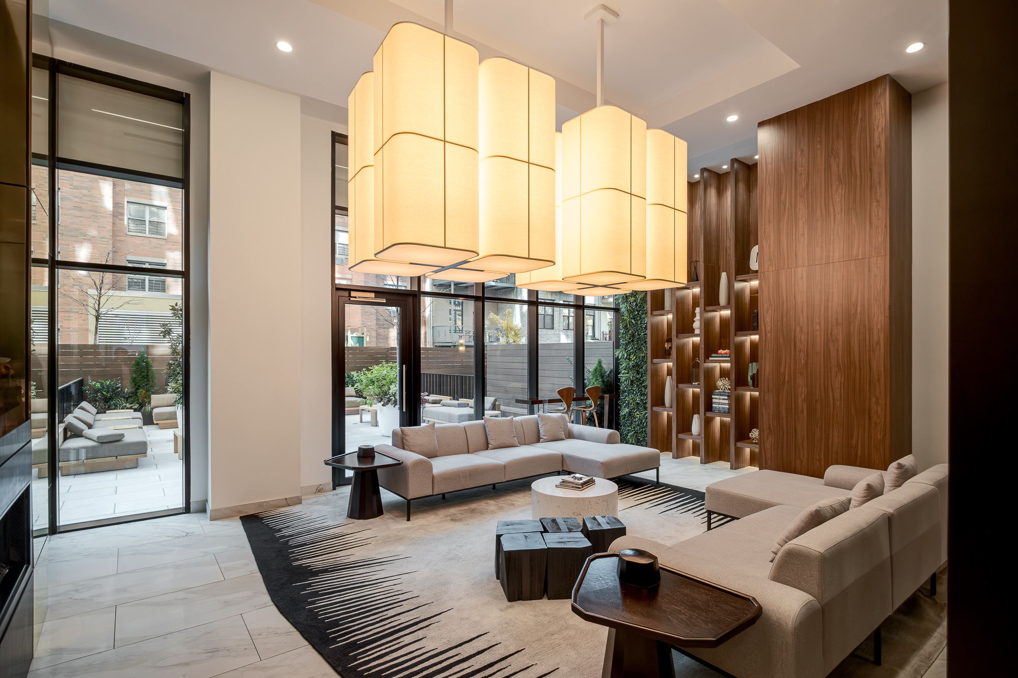 Double-height residents lounge with lantern pendants and walnut library wall