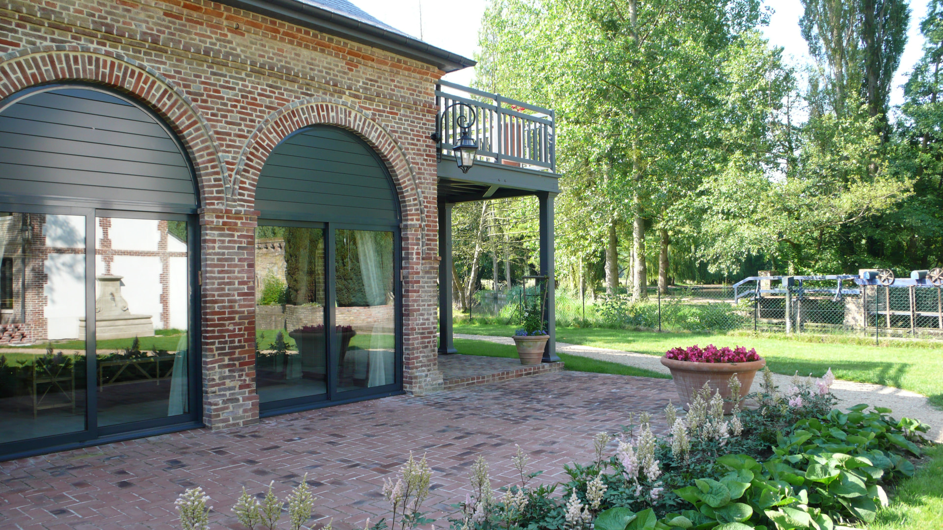 Brick arcade with full-height glazed arched doors opening onto a paved garden terrace