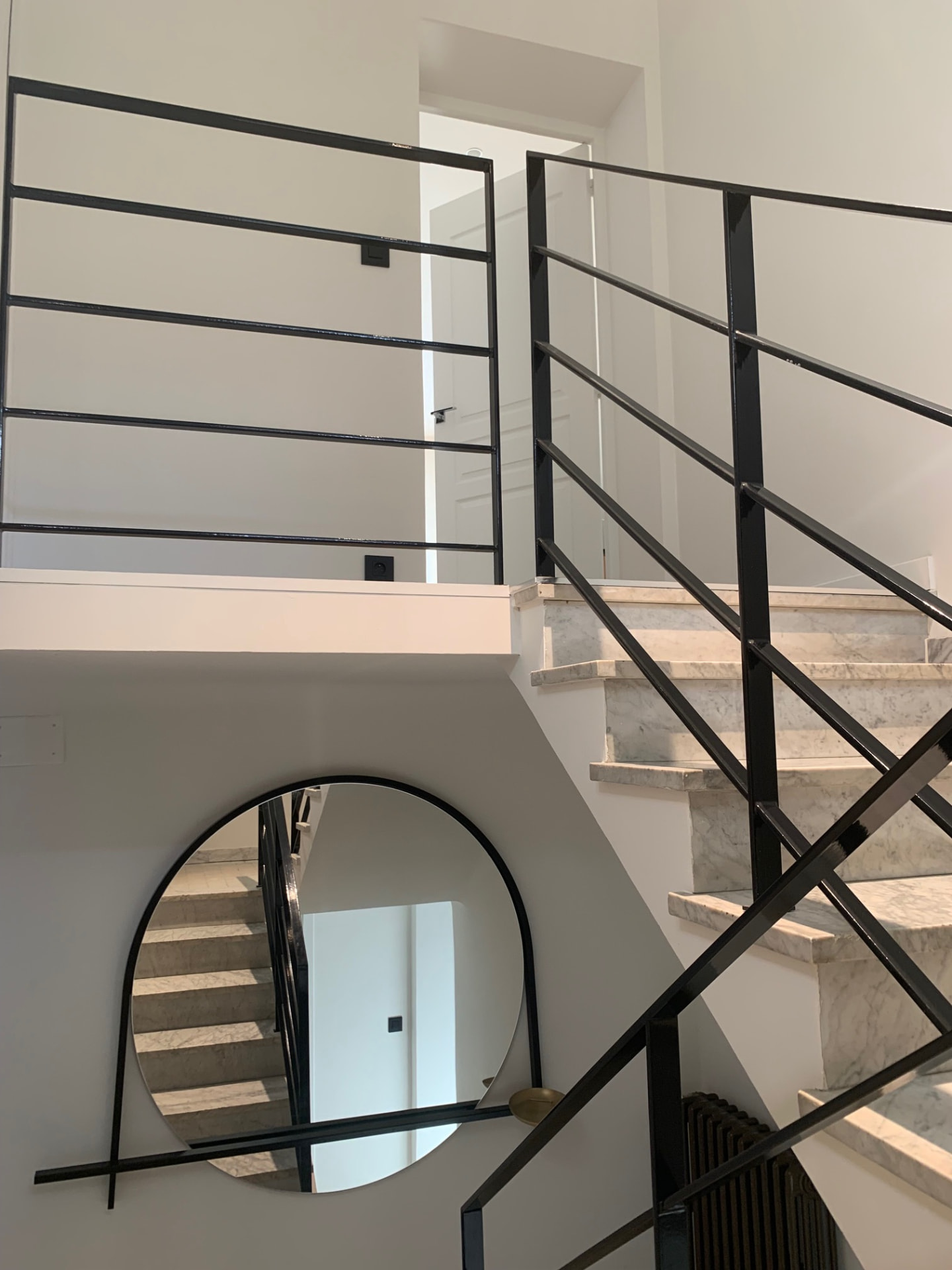 Marble stair with black steel railing and a round mirror