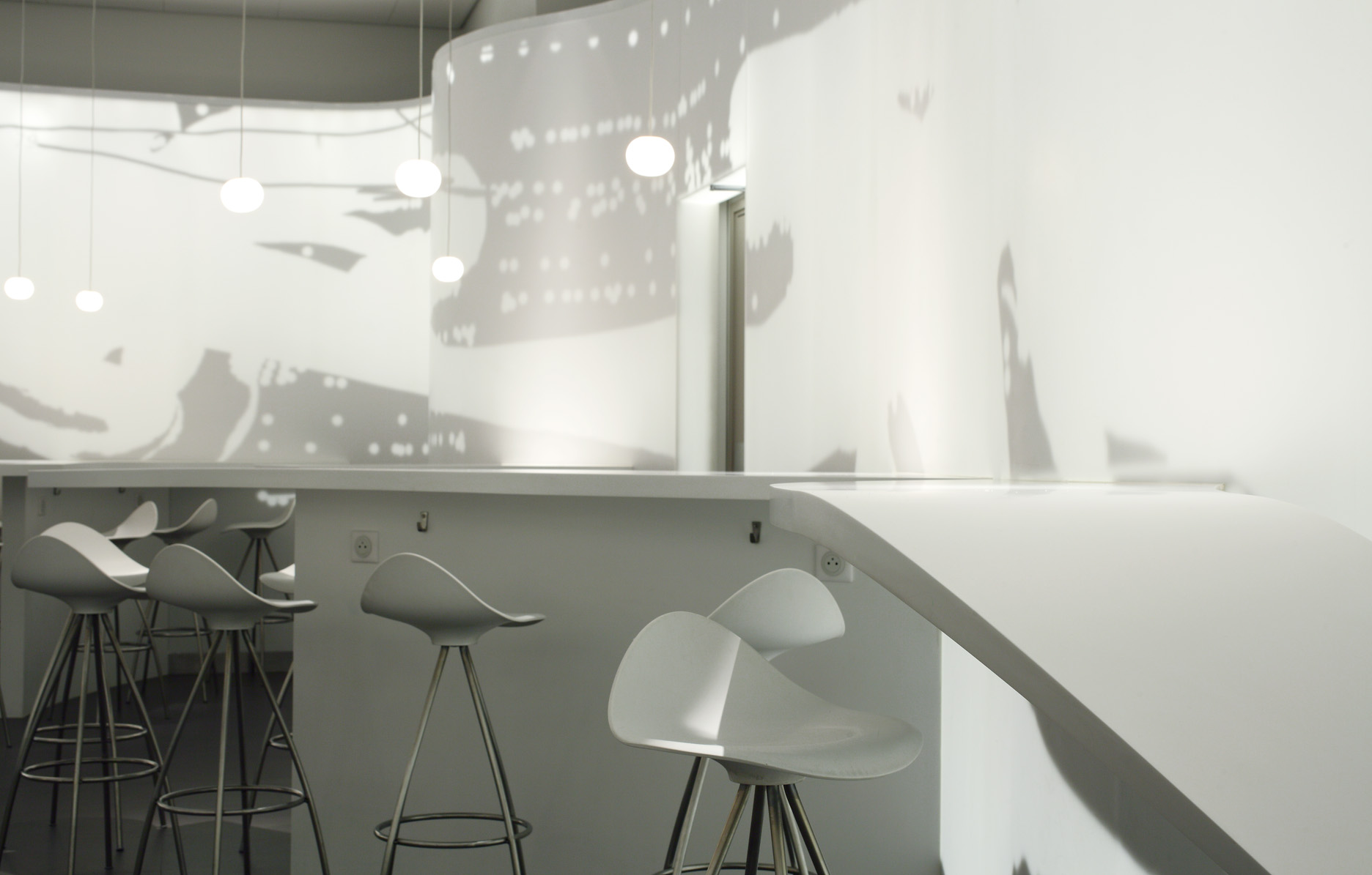 Row of white bar stools along the serpentine counter beneath pendant globes