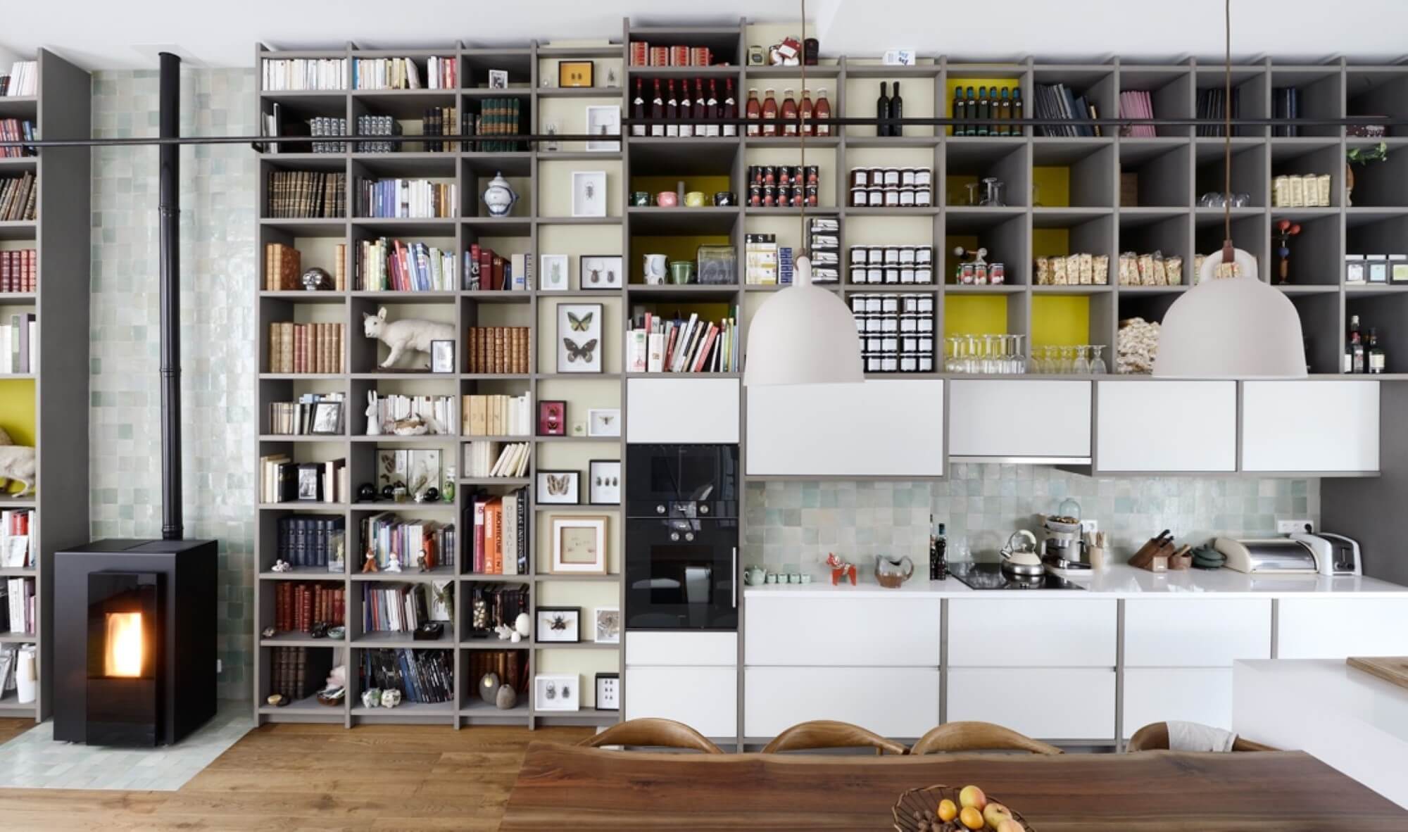 Full-height bespoke grey shelving system with zellige-tiled chimney breast, wood stove and open kitchen