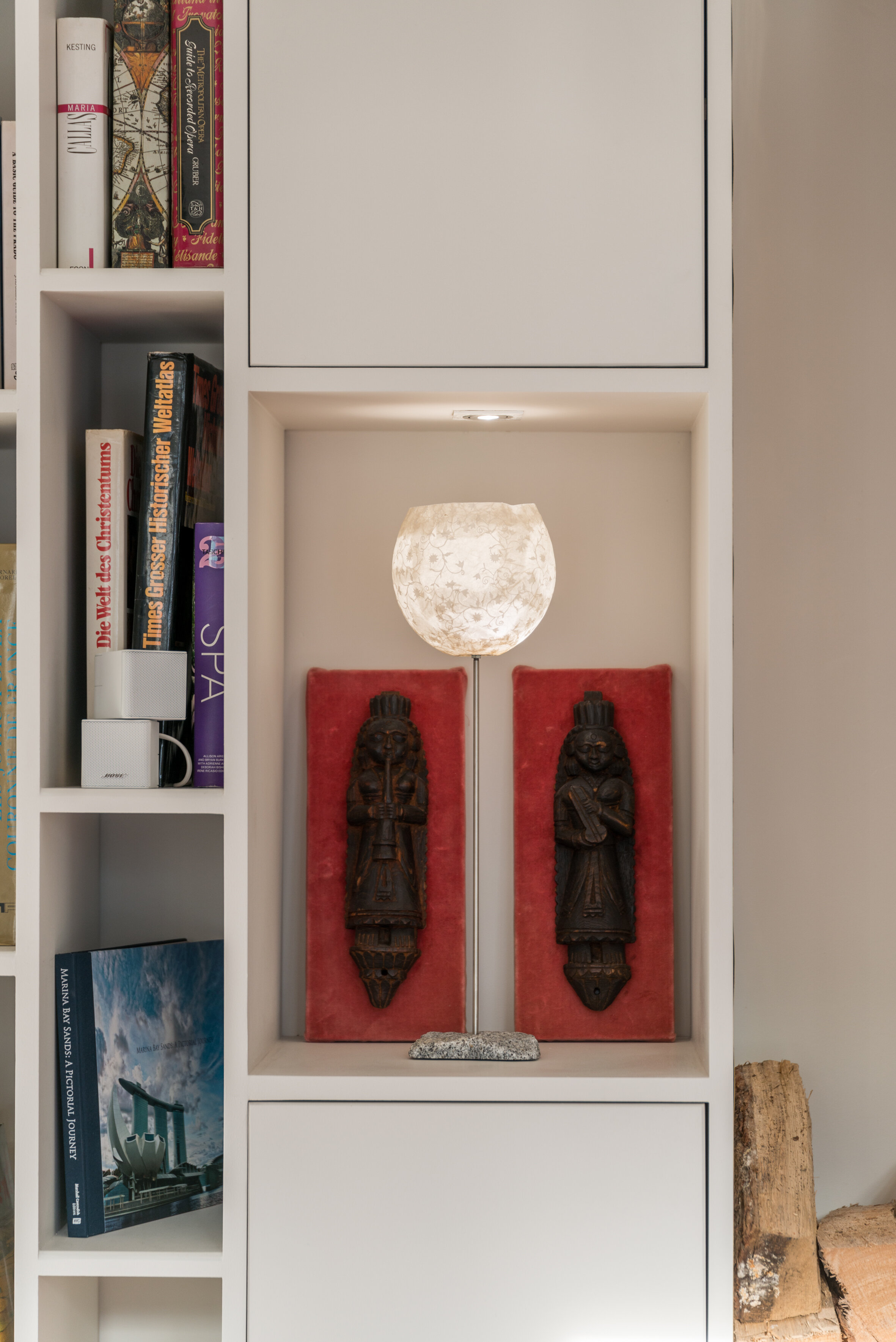 Bookshelves and a lit niche with an alabaster lamp and carved figures on red panels