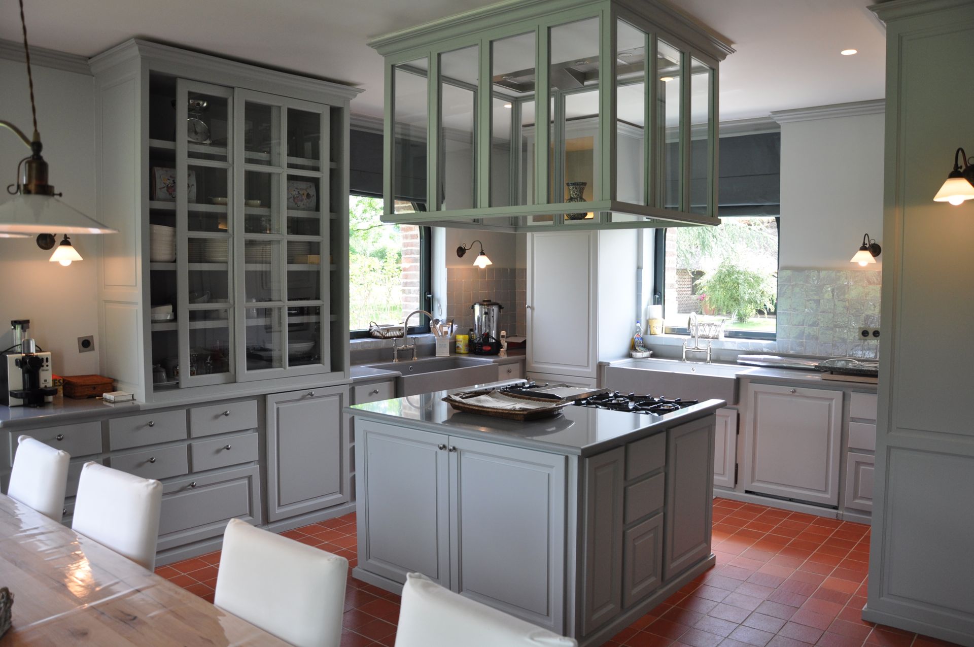 Bespoke grey-green painted kitchen with glazed lantern hood and terracotta floor in a Normandy manor house